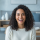 A happy young woman with dark, curly hair smiling at the camera, conveying trust and satisfaction.